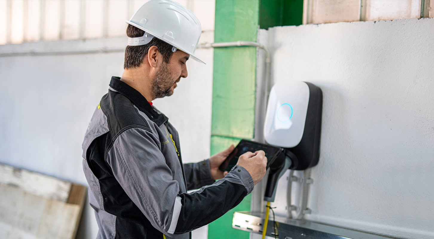 A man wearing a hard hat and jacket is focused on operating an electric charging device.